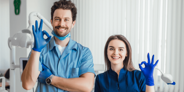 photo-smiling-dentist-standing-with-arms-crossed-with-her-colleague-showing-okay-banner-3